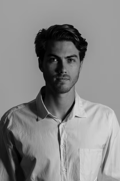 A black and white headshot of a man posing against a solid-colored wall