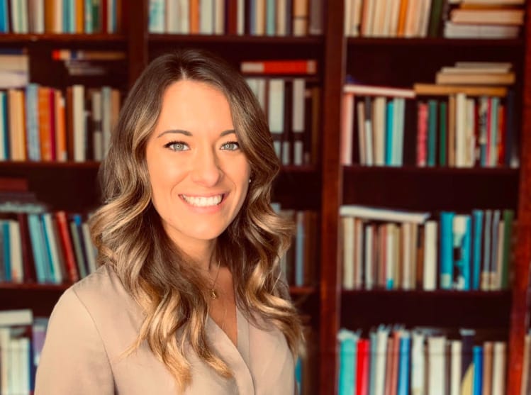 A woman in a library posing for a professional headshot wearing a solid color top