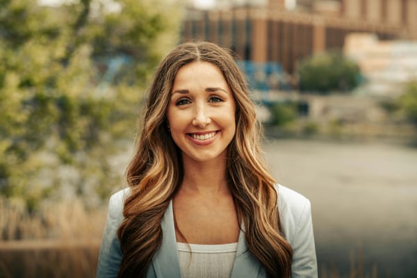 A professional headshot of a woman posing in an outdoor setting 